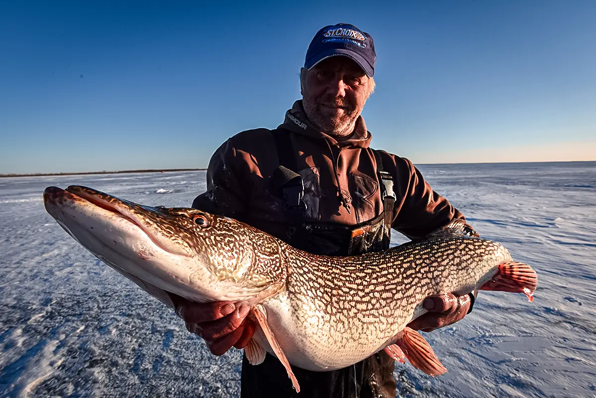 man holding pike on the ice