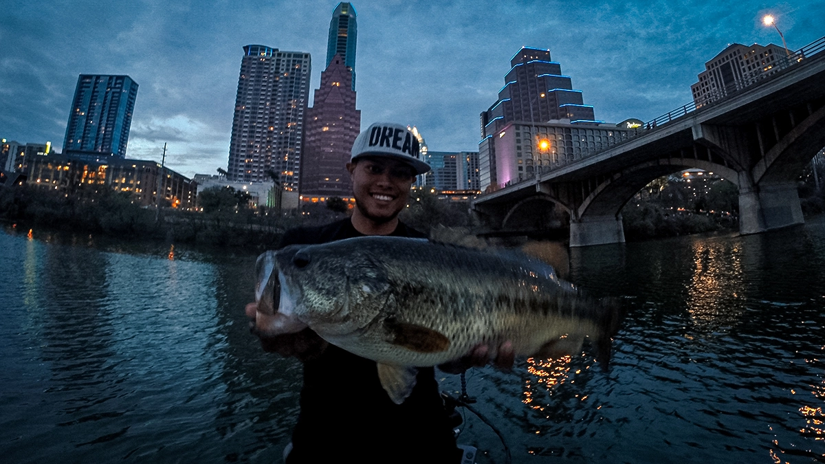 oliver ngy with a big bass on a river with a city in the background