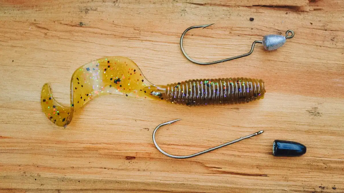 a curly tail grub on a wood table with hooks and jig heads