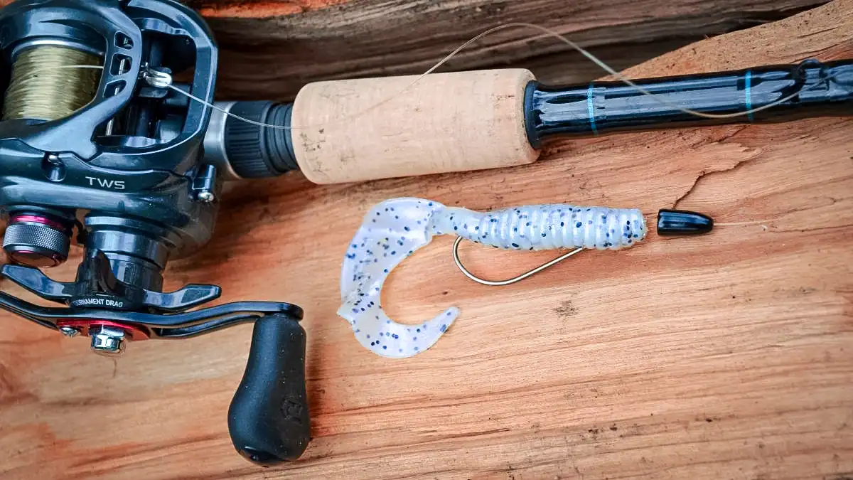 a curly tail grub on a hook wood table with a rod reel