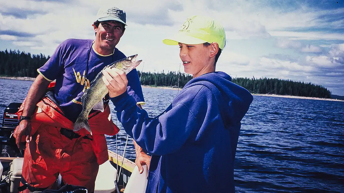 young angler holding a walleye with his dad in background