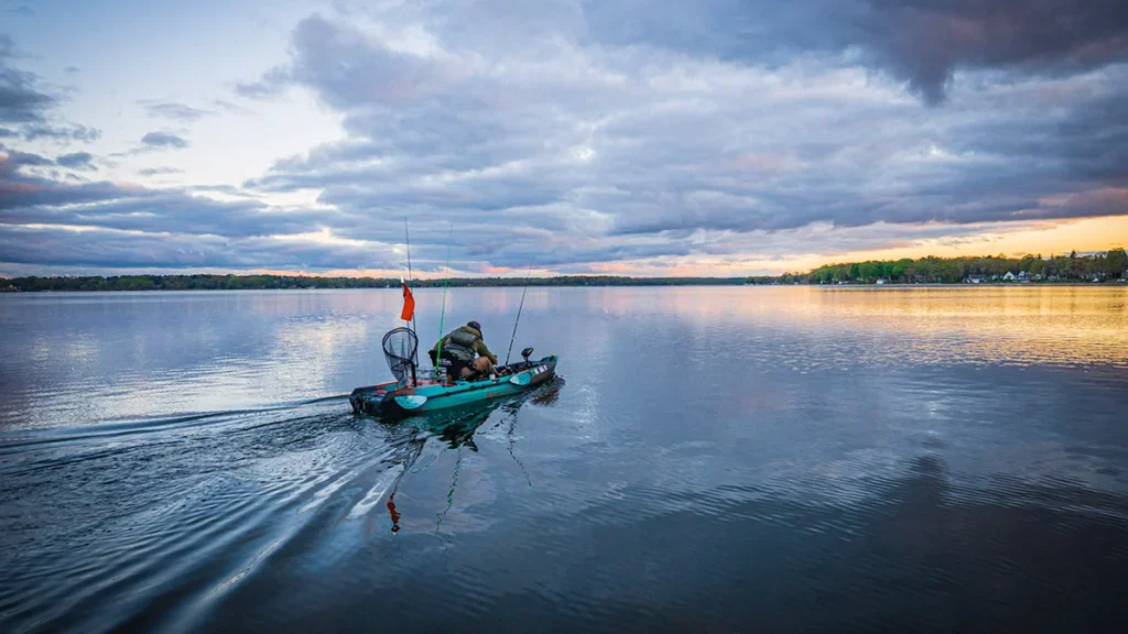 An angler on a fishing kayak motors toward the horizon.