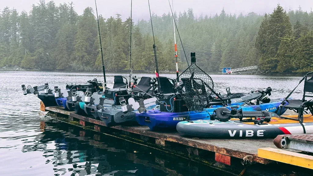 Vibe kayaks lined up on a dock with a foggy treeline in the background.