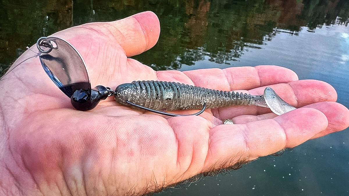 A closeup of an SPRO Blade Swing jig head held in an open palm over the water.