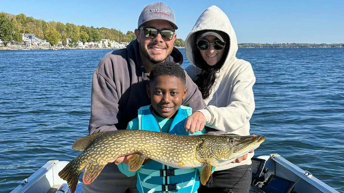 A child with two adults behind him smiles as he holds up a fish
