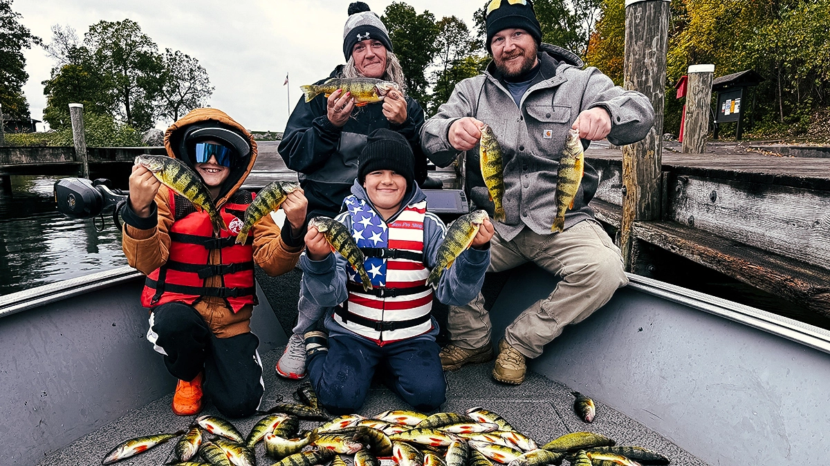 A family of four holds up some of the fish they caught with a pile of fish in front of them