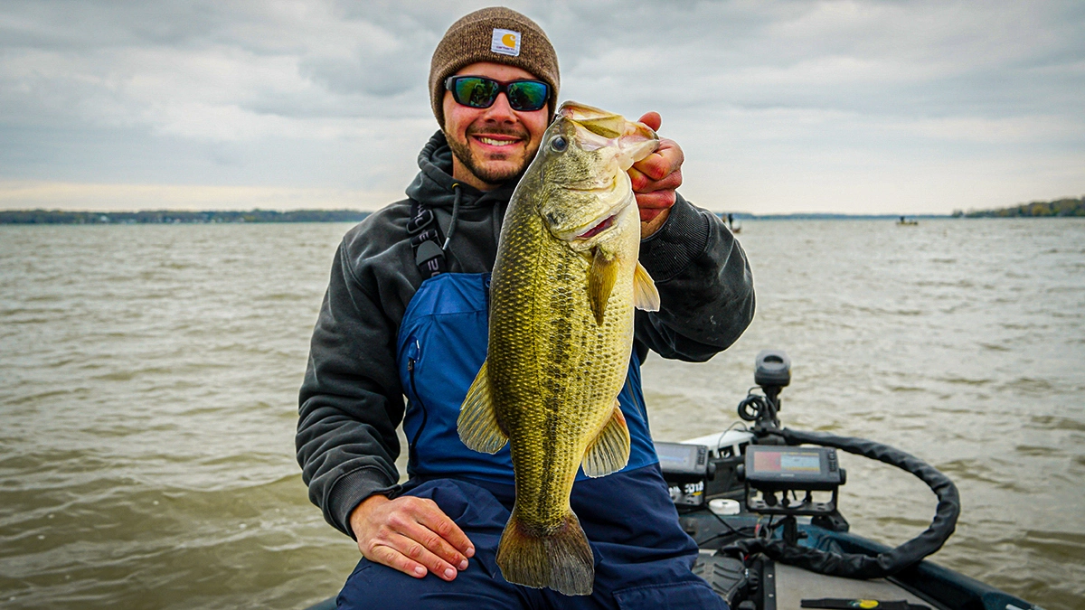 A man in colder-weather gear on a boat holds a bass