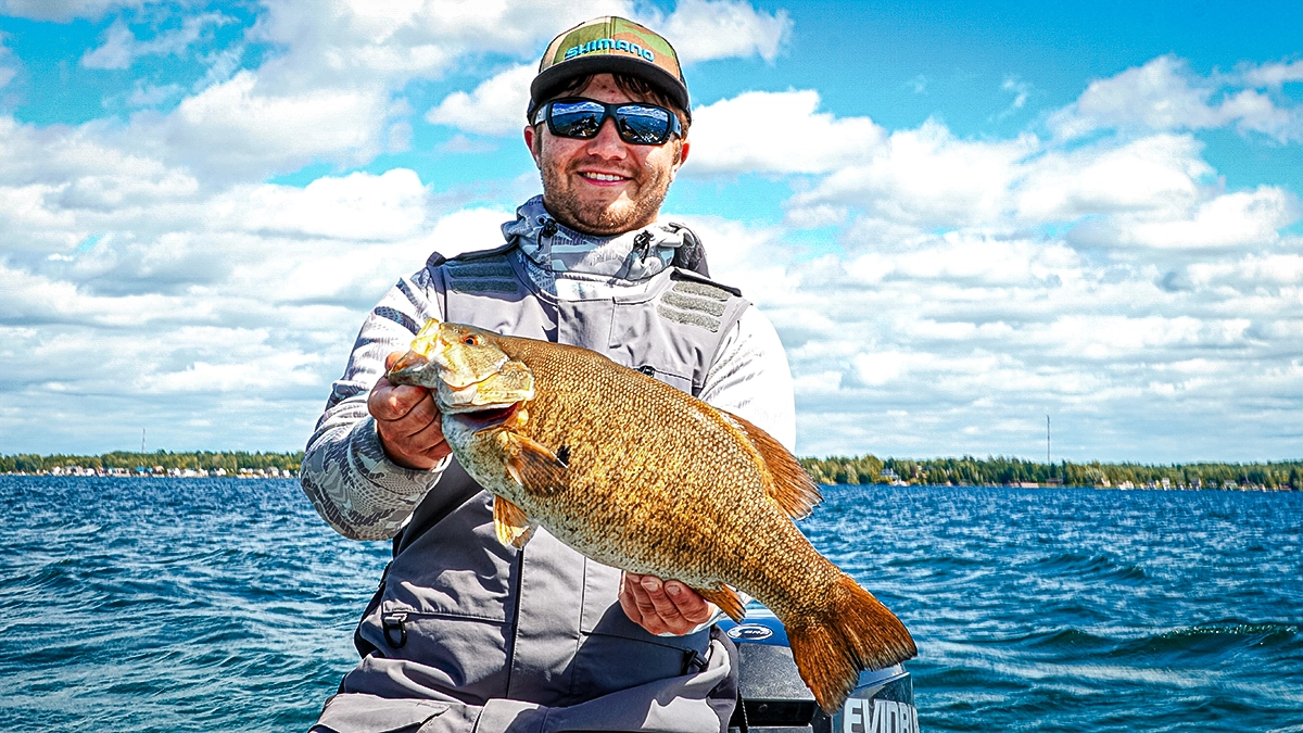 A man on the water holds up a fish, with the landline off in the distance.
