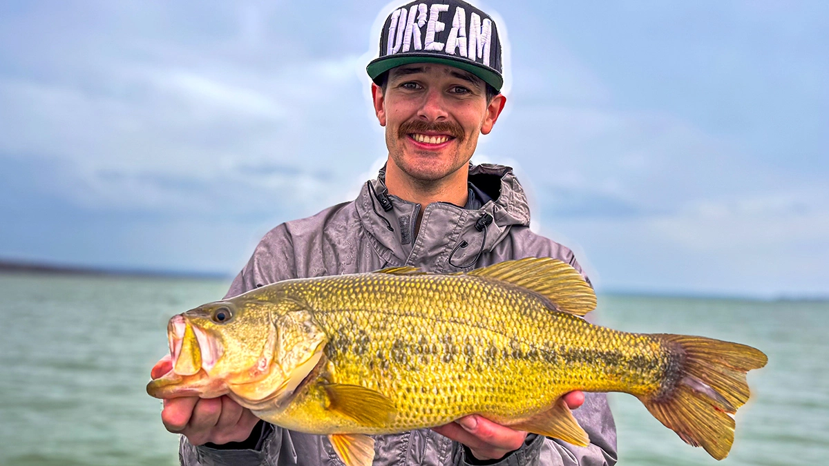 A man in a hat holds up a bass, with the water and sky meeting at the horizon off in the distance