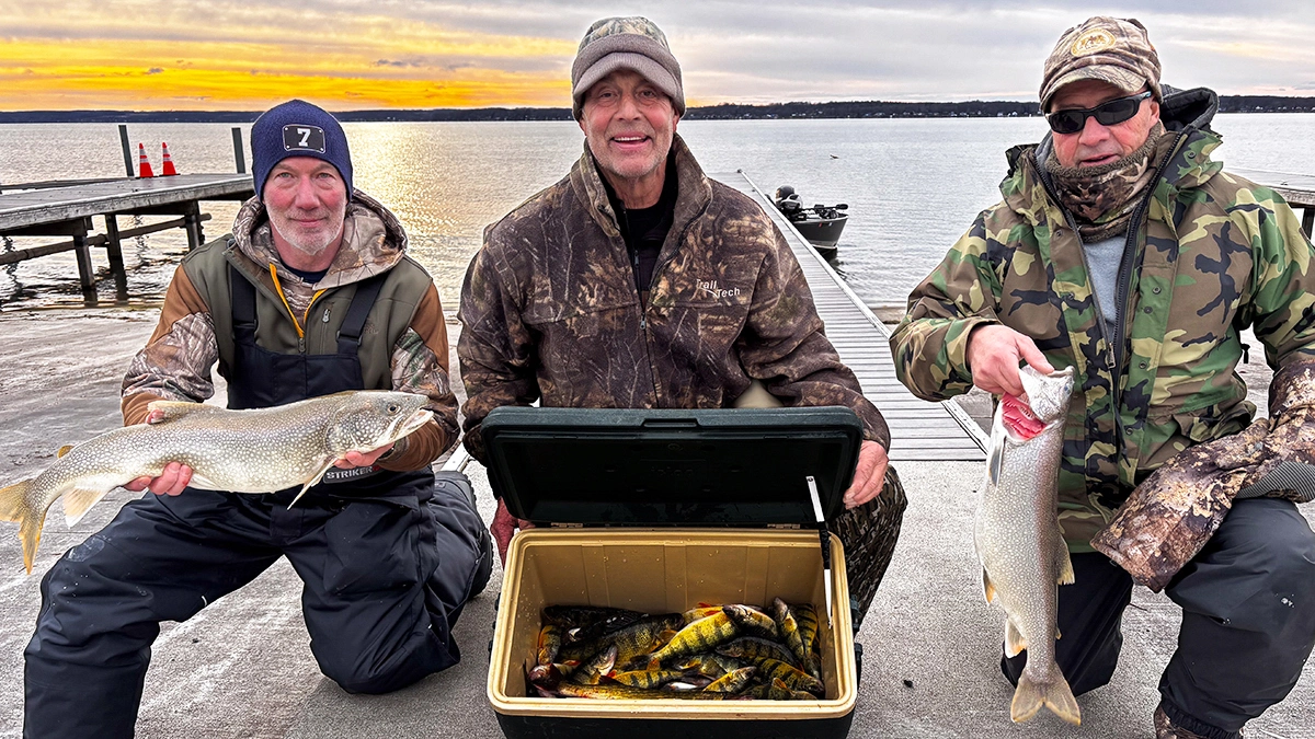 Three men show off the fish they caught, including a cooler with perch inside