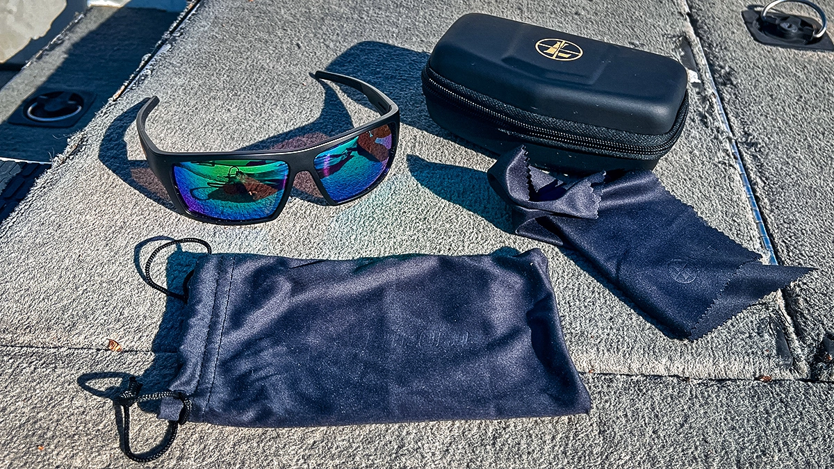 A pair of Leupold Performance Eyewear Switchback Sunglasses with the emerald mirror lenses positioned on the dock of a boat with the case, baggie and cleaning cloth included with them.