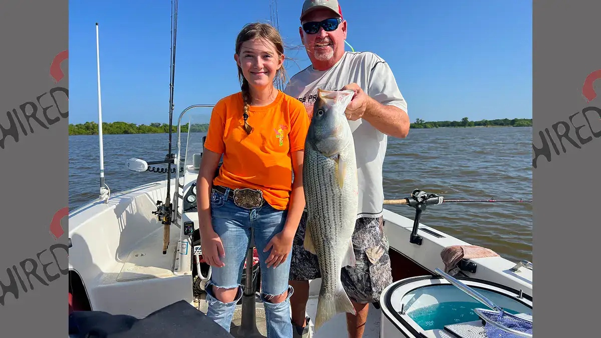 Two people on a boat with a freshly caught striper.