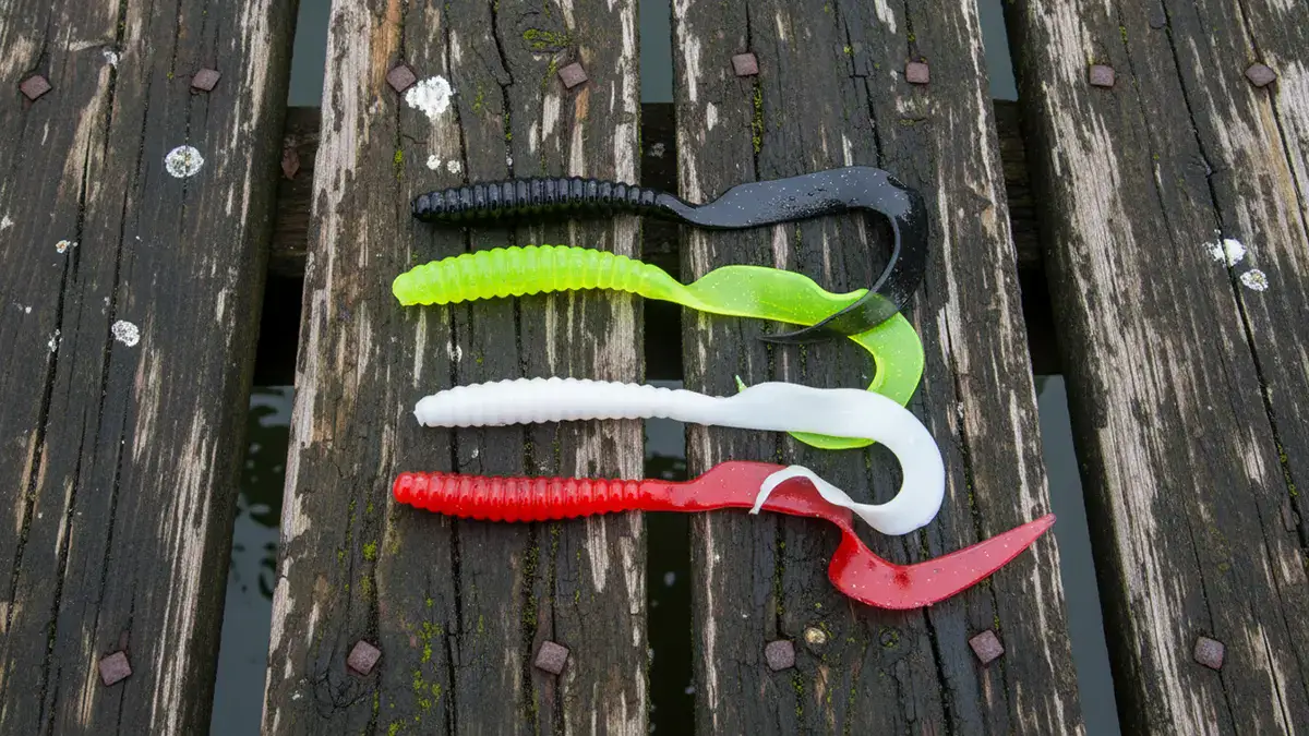 Four Mister Twister Twister Tail lures displayed on a wet dock