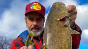 Roy Bilby holds a curly-tail grub in one hand and a fish in another.