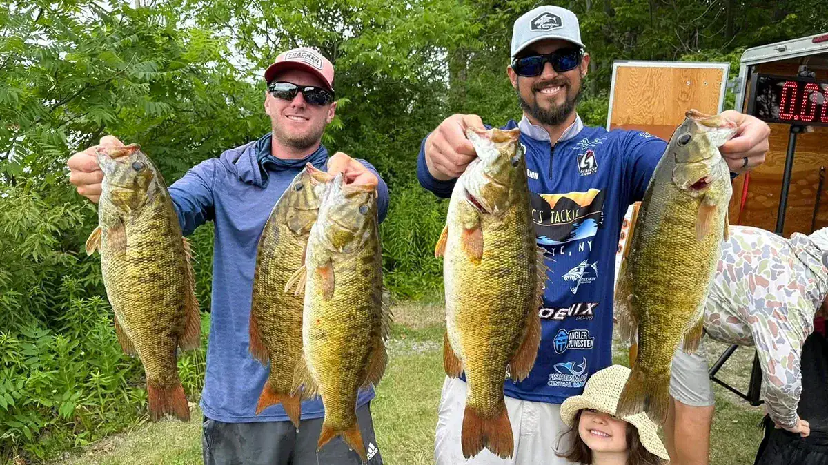 Two anglers hold up a total of five fish, with verdant foliage behind them.