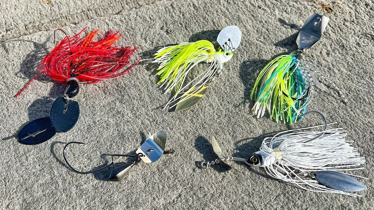 A photo of five vibrating jigs: an ABT Lures Original I-Vibe Bladed Jig; a D&M Custom Baits Chopper Swim Jig; the Fish Head Primal Vibe Jig; the Decoy Zero-Dan Flash Bladed Jig; and the Teckel USA Bladewaker Bladed Jig 1/2oz bait.