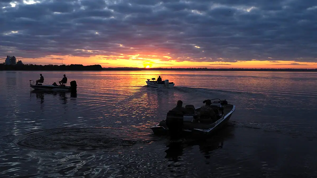 Fishing boats head toward a sun that's just over the horizon.