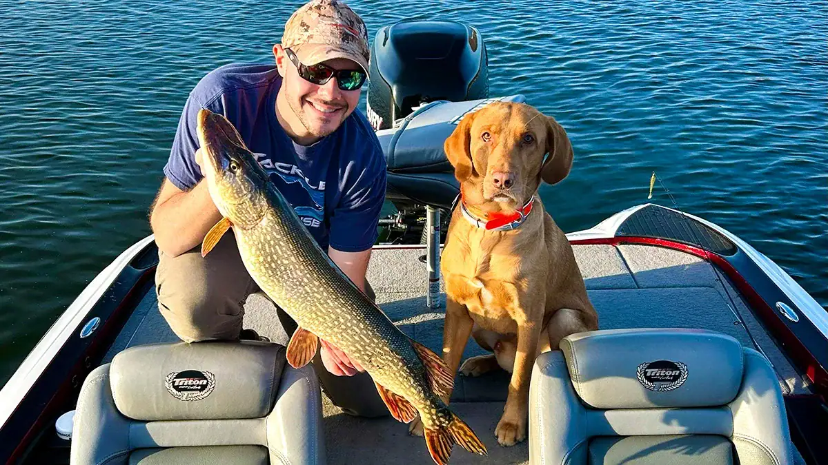 A man, a dog, and an early-season Northern Pike on a boat.