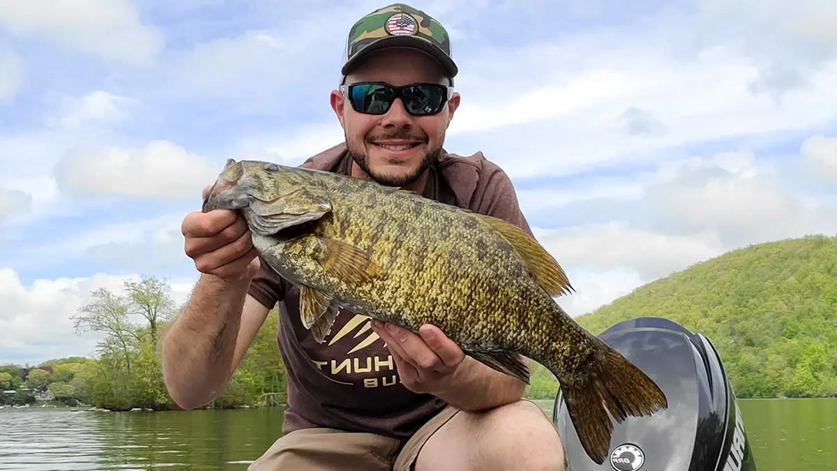 Man near a boat motor holds up a bass caught with one of the top five bait for post-spawn smallmouth success.