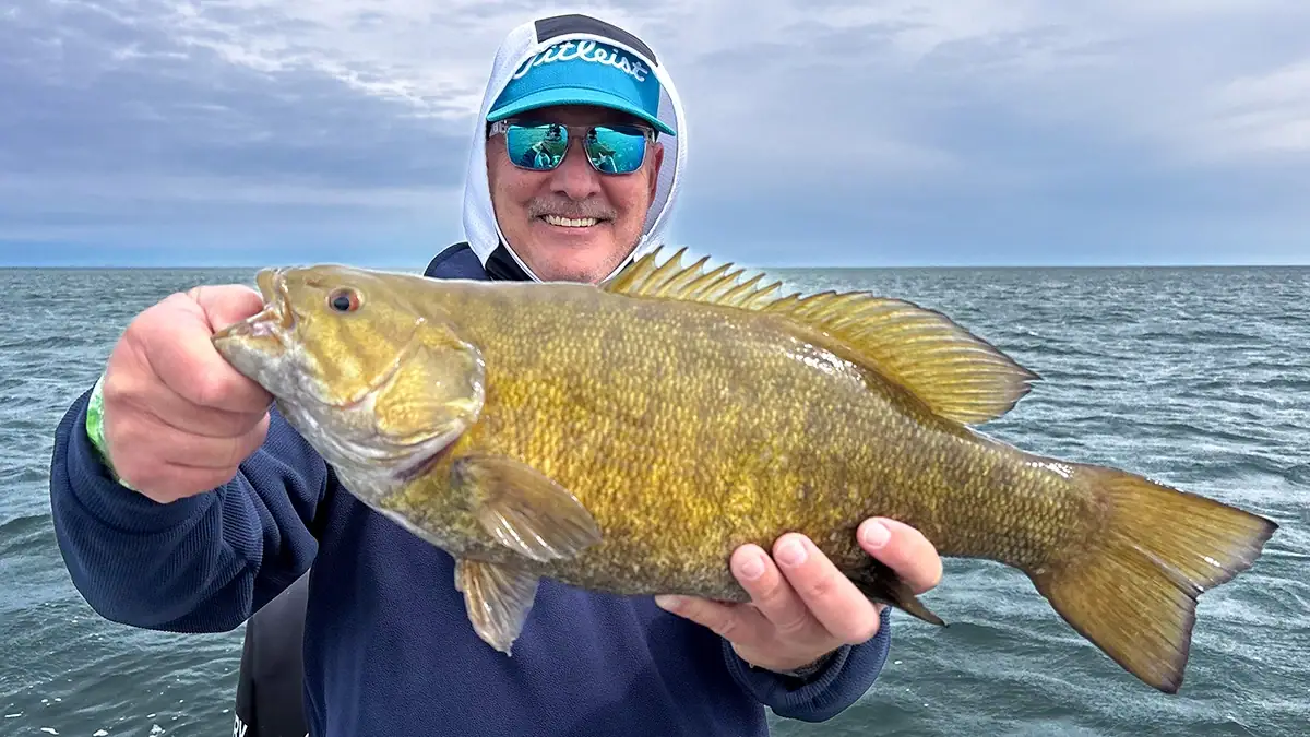 A man on the water shows off a bass caught with one of the top five bait for post-spawn smallmouth success.
