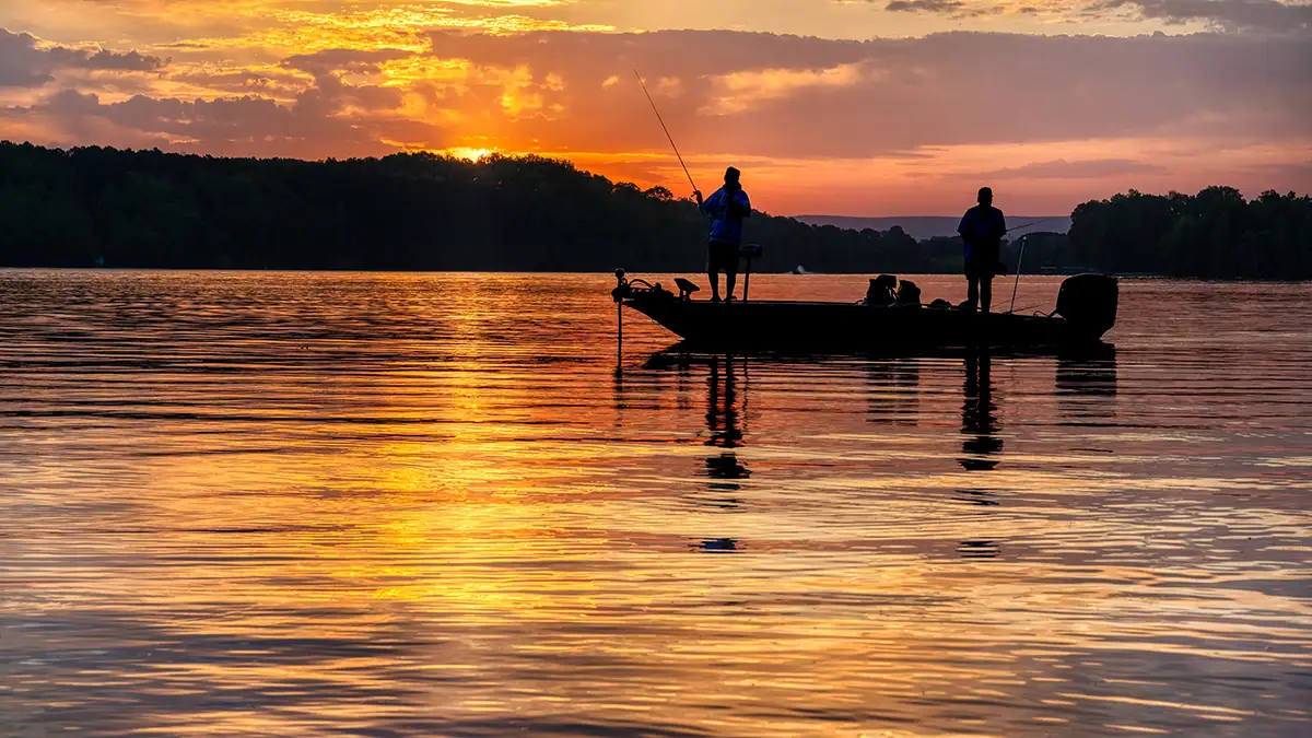 Two anglers fishing at sunrise on the water.
